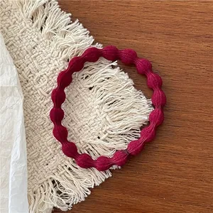 Detailed view of dark red elastic hair tie with textured finish on a cream tassel mat