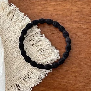 Detail view of a black wavy high-elasticity hair tie placed on a woven cotton mat