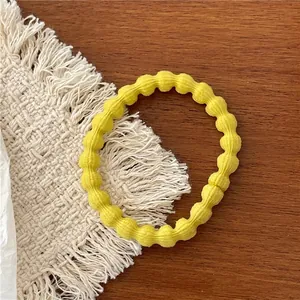 Detail of yellow elastic hair tie with soft knit sphere texture on a wooden surface