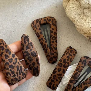Leopard print fabric hair clips in various geometric shapes on a stone textured background
