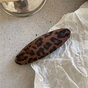 Detailed view of a soft leopard print fabric hair clip on a minimalist textured surface