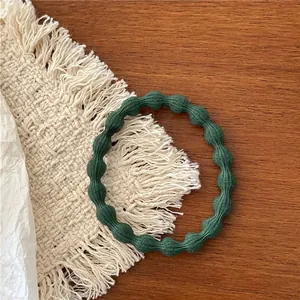 Close-up of a dark green elastic hair tie with a textured wave bead pattern on a wood surface
