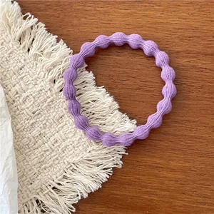 Detailed close-up of a purple elastic wavy hair tie placed on a stylish woven coaster