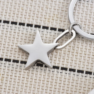 Polished silver stainless steel star keychain accessory with round keyring on woven mat