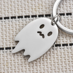 Polished silver stainless steel ghost keychain with hollow cutout on woven background