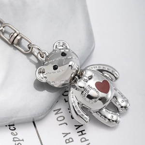 Silver bear keychain with red heart and stitched detail on marble and magazine background