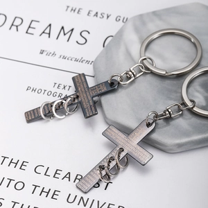 Close-up of black and silver stainless steel cross keychain with engraved scripture