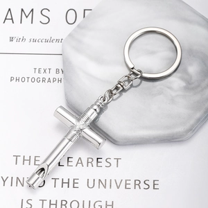 Detailed view of silver cross whistle keychain with polished metal texture on marble