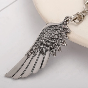 Retro antique silver angel wing keychain with detailed feather texture on white ceramic