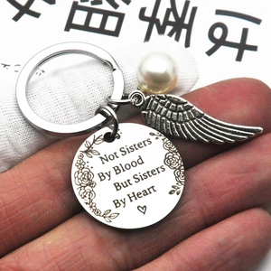 Close-up of stainless steel keychain with Not Sisters By Blood engraving and pearl wing charms