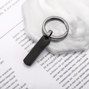 Minimalist matte black stainless steel rectangle pendant keychain on marble pedestal