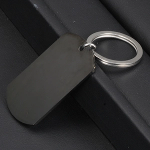 Black polished stainless steel dog tag keychain with silver metal ring on leather background