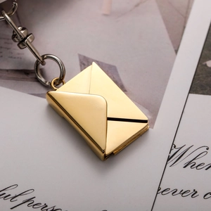 Polished gold envelope keychain with pull-out card detail on vintage postcard background