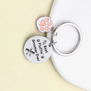Dog groomer keychain with pink paw charm and engraved round metal tag on a display stand