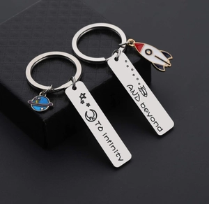 Close-up of rocket and planet couple keychains with To infinity AND beyond engraving