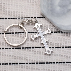 Retro silver cross keychain with white enamel inlay and four crystals on a woven mat