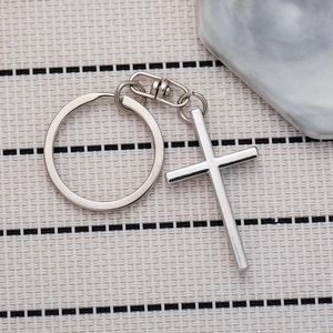 Close-up of a polished silver metal cross keychain with a lobster clasp on a woven mat