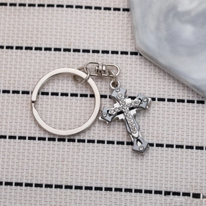 Three-layer silver cross keychain with sparkling rhinestones on a beige woven surface