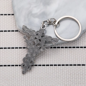 Vintage silver metal keychain with double dragon and cross design on a stone surface