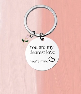 Detail of stainless steel keychain with pink rose charm and engraved romantic text