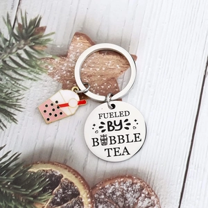 Stainless steel bubble tea keychain with Fueled by Bubble Tea charm on white wood