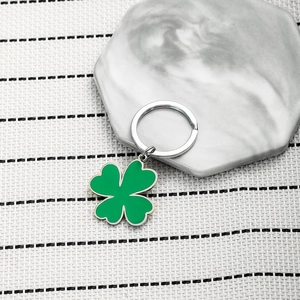 Detail of green four-leaf clover keychain with silver metal ring on marble surface