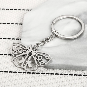 Minimalist hollow moth stainless steel keychain with crescent moon detail on marble surface