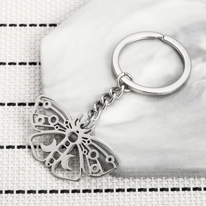 Sleek stainless steel moth keychain with celestial moon cutouts on marble surface