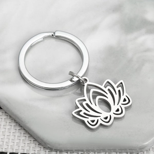 Minimalist silver lotus flower stainless steel keychain on marble and woven background