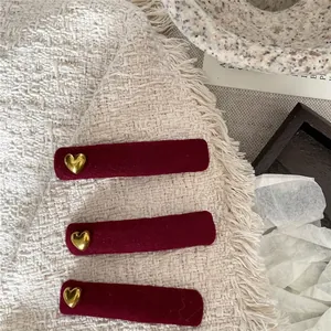 Three red velvet rectangle hair clips with golden heart accents on a tweed surface