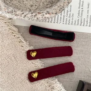 Set of 3 burgundy velvet hair clips with golden heart accents on a beige knit background
