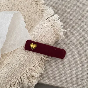 Macro shot of burgundy velvet hair clip with a small gold heart detail on white fabric