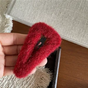 Detailed view of dark red plush hair clip with soft fuzzy texture on a warm wooden base