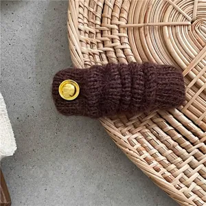 Dettaglio del fermaglio per capelli in maglia marrone scuro con bottone metallico dorato