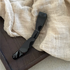 Glossy black banana hair clip with elegant bow design on natural linen and wood