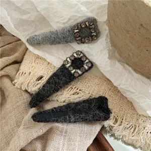 Detail of grey knitted hair clips with square rhinestones on a warm textured background
