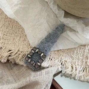 Detailed view of grey plush hair clip with square rhinestone accents on soft knit fabric
