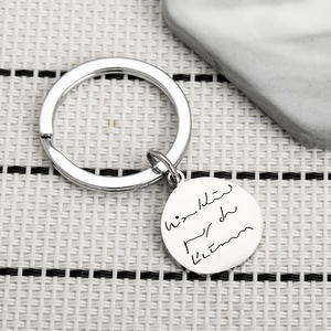 Minimalist silver stainless steel round keychain with custom text on a textured stone