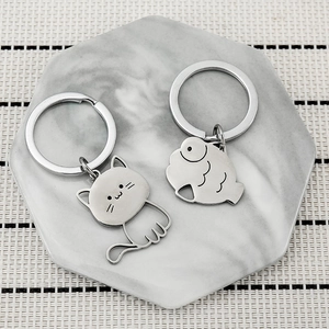Set of two silver cat and fish stainless steel keychains on marble display tray