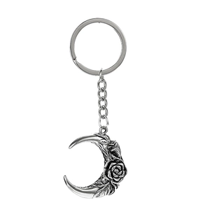 Macro shot of retro silver crescent moon keychain with rose engraving detail on white background