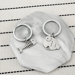 Polished stainless steel fish bone and cat fish keychains on marble display plate