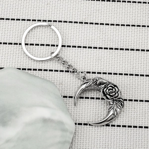 Silver crescent moon keychain with embossed rose pattern on a minimalist textured background