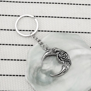 Vintage silver crescent moon keychain with rose relief detail on marble tray