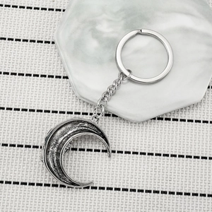 Vintage silver crescent moon keychain with textured metal surface on a striped background