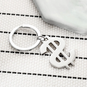 Polished stainless steel dollar sign keychain with silver split ring on marble decor