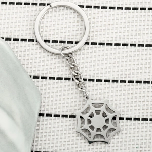 Detailed macro view of a silver stainless steel spider web keychain on a textured background