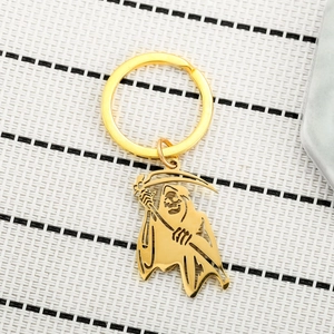 Detailed view of a gold-tone Grim Reaper scythe keychain with intricate cutout metalwork