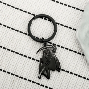 Detailed view of a matte black Grim Reaper scythe keychain on a textured background
