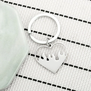 Detailed view of silver heart flame keychain with polished hollow design on woven texture