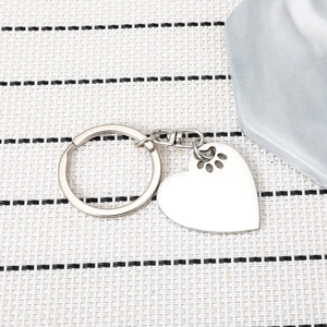 Silver stainless steel heart keychain with hollow paw print on a textured background